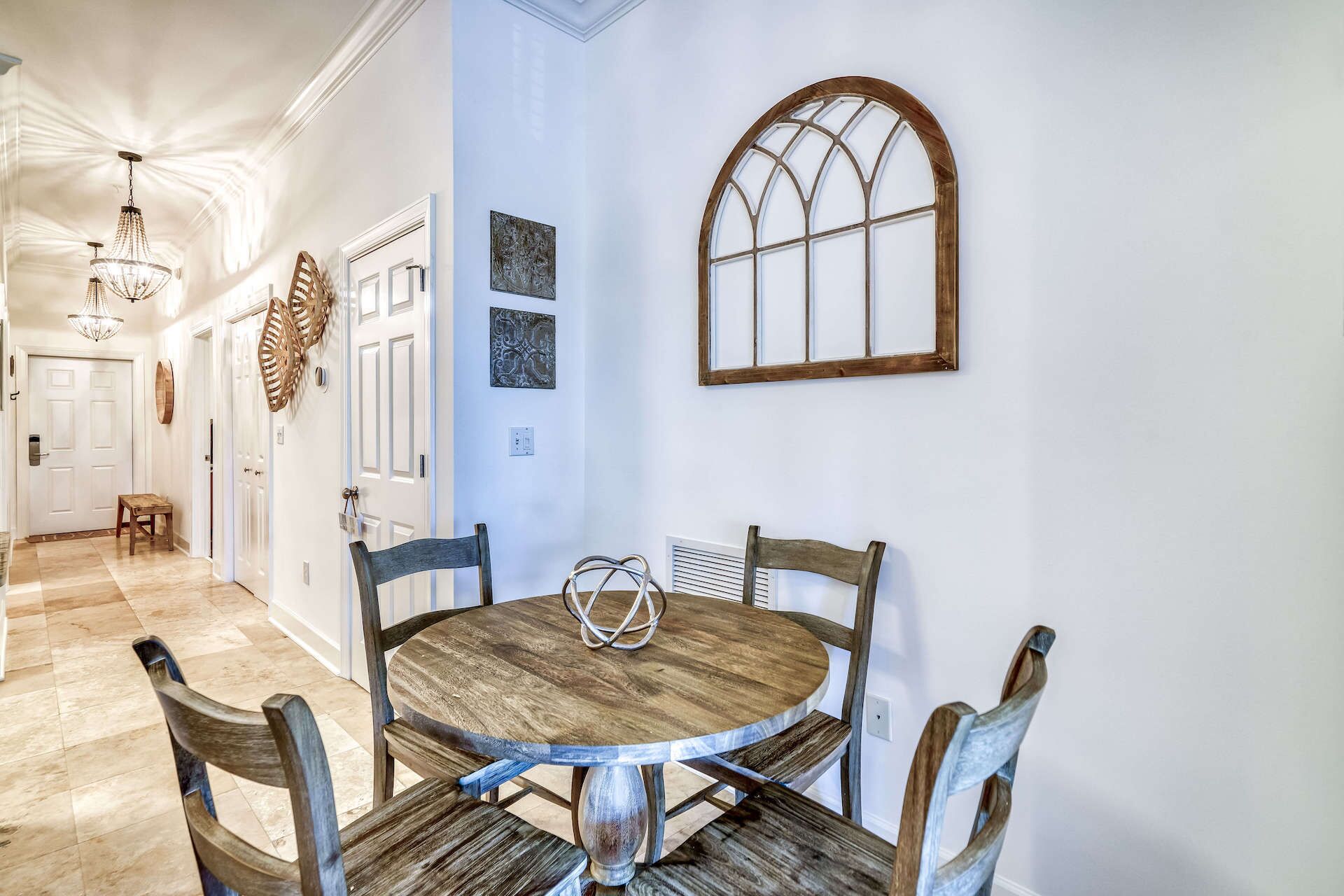 Un comedor con una mesa redonda de madera y sillas, una araña y un ventanal decorativo.