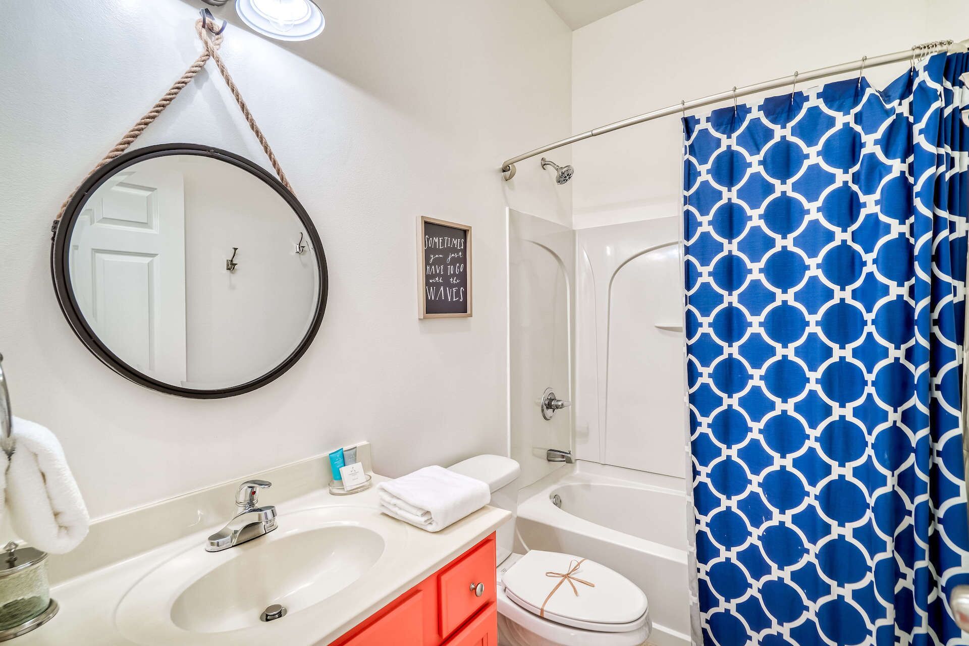 A bathroom with a round mirror, a sink, a toilet, a bathtub, and a shower curtain.