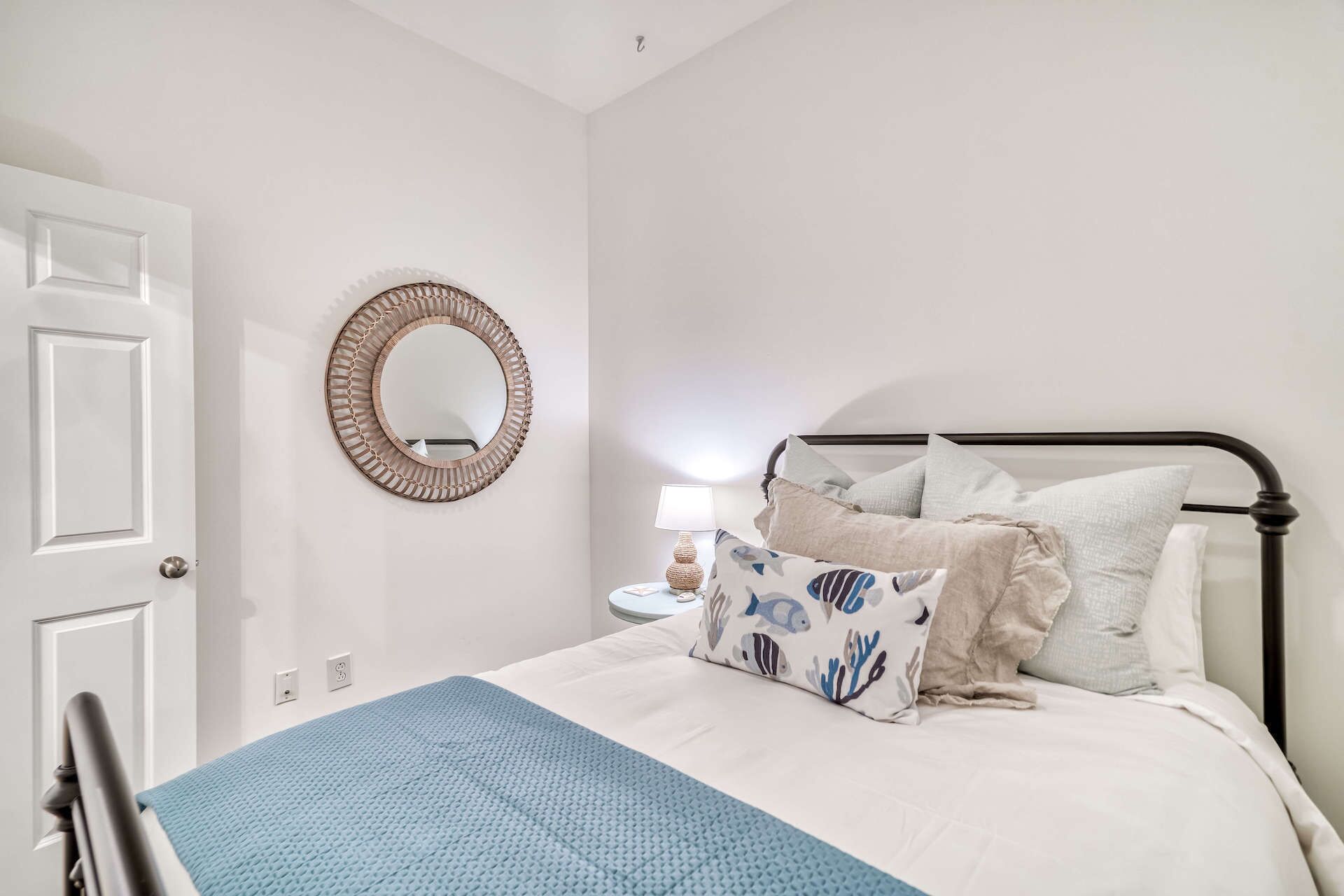 Un dormitorio con cama, almohadas, una lámpara de noche, un espejo en la pared y una puerta.