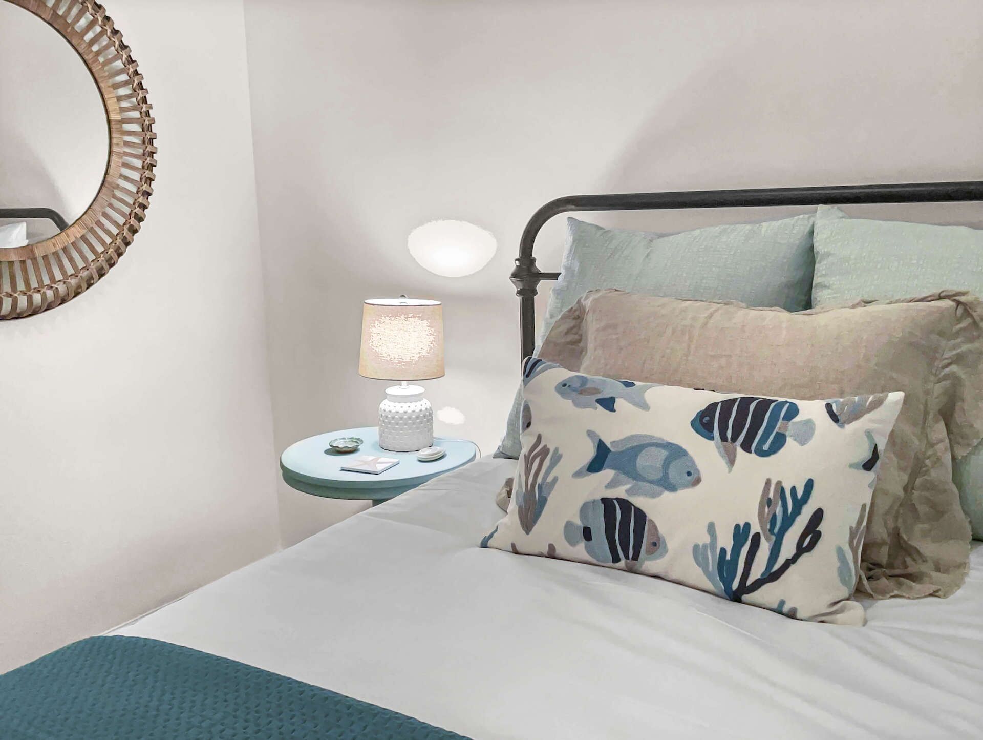 A bedroom with a bed, a bedside table with a lamp, and a round mirror on the wall.