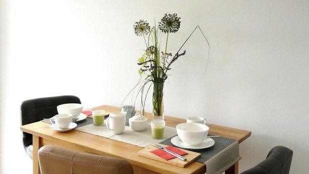 Una mesa de comedor con un jarrón de flores, varias tazas, una jara y una tetera.