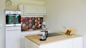 Una cocina compacta con armarios blancos, horno de acero inoxidable, salpicadero colorido, cafetera y hervidor en la encimera.