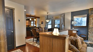 A cozy living room with a wooden bench, a dining area with a table and chairs, and a kitchen in the background. - Ridge Retreat Breckenridge Townhome: Great Location, Views (Breckenridge)