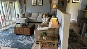 Un salon avec un canapé, une table basse et une lampe. Des tableaux encadrés ornent le mur et une plante en pot est posée sur la table basse.