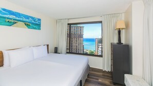 A hotel room with a large bed, a nightstand, a lamp, and a view of the ocean and buildings. - Discovery Bay deluxe ocean view, near Ala Moana Shopping Center & the beach! (Honolulu)