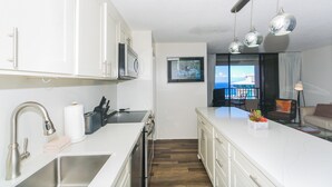 A modern kitchen with white cabinets, a stainless steel sink, and a built-in oven. There is a dining area with a view of the sea. - Discovery Bay deluxe ocean view, near Ala Moana Shopping Center & the beach! (Honolulu)
