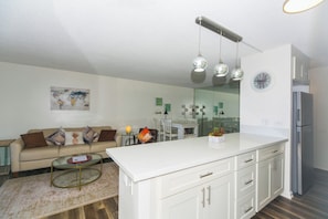 A modern kitchen with white cabinets, a stainless steel refrigerator, and a dining area with a white table and chairs.