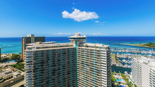 A high-rise hotel with a central tower, multiple balconies, and a marina with boats in the background. - Discovery Bay deluxe ocean view, near Ala Moana Shopping Center & the beach! (Honolulu)