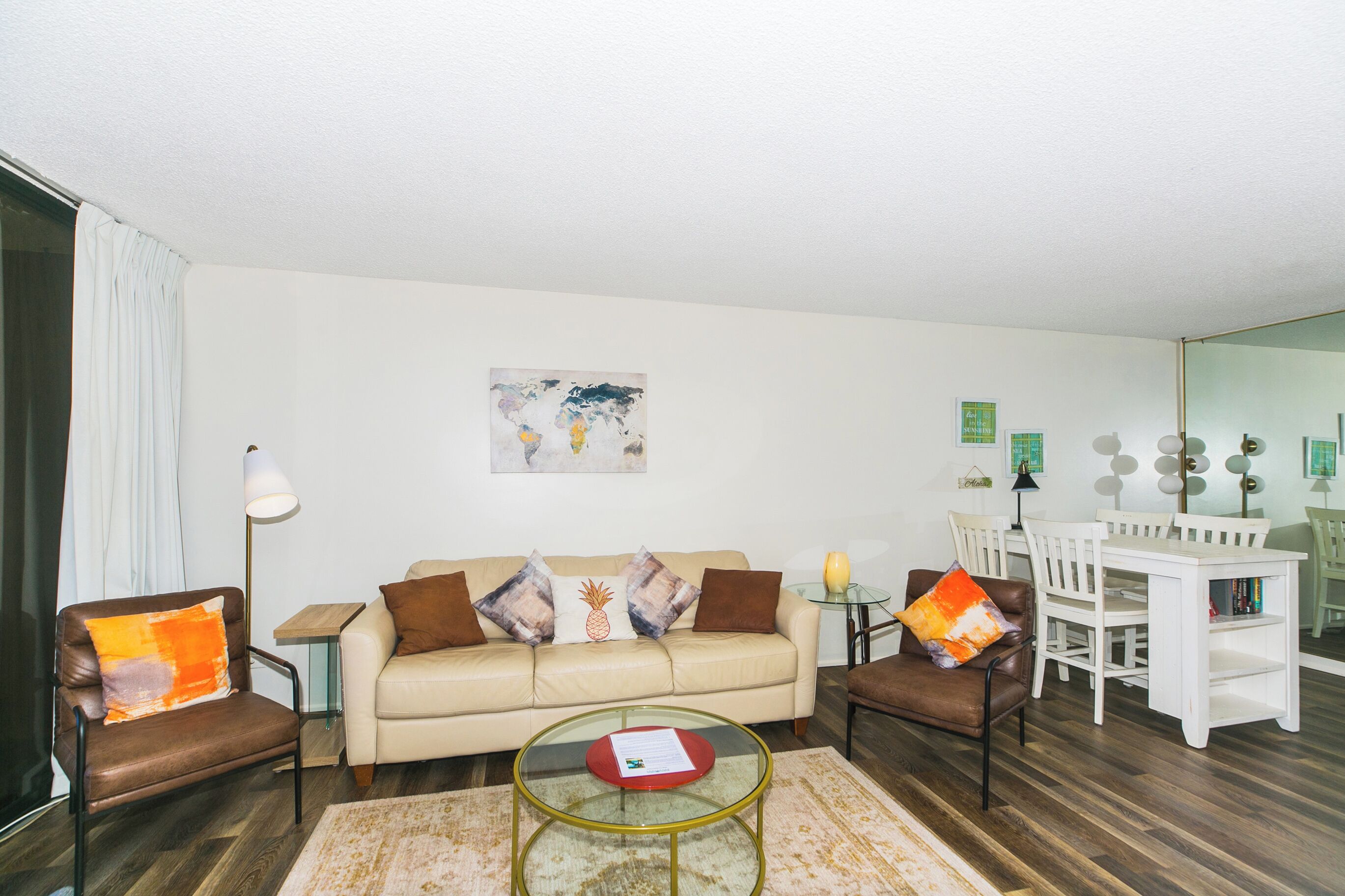 Un salon comprenant un canapé, deux fauteuils, une table basse, une table à manger avec des chaises et un tableau accroché au mur.
