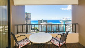 A balcony with a round table and two chairs, overlooking a cityscape and the ocean. - Discovery Bay deluxe ocean view, near Ala Moana Shopping Center & the beach! (Honolulu)