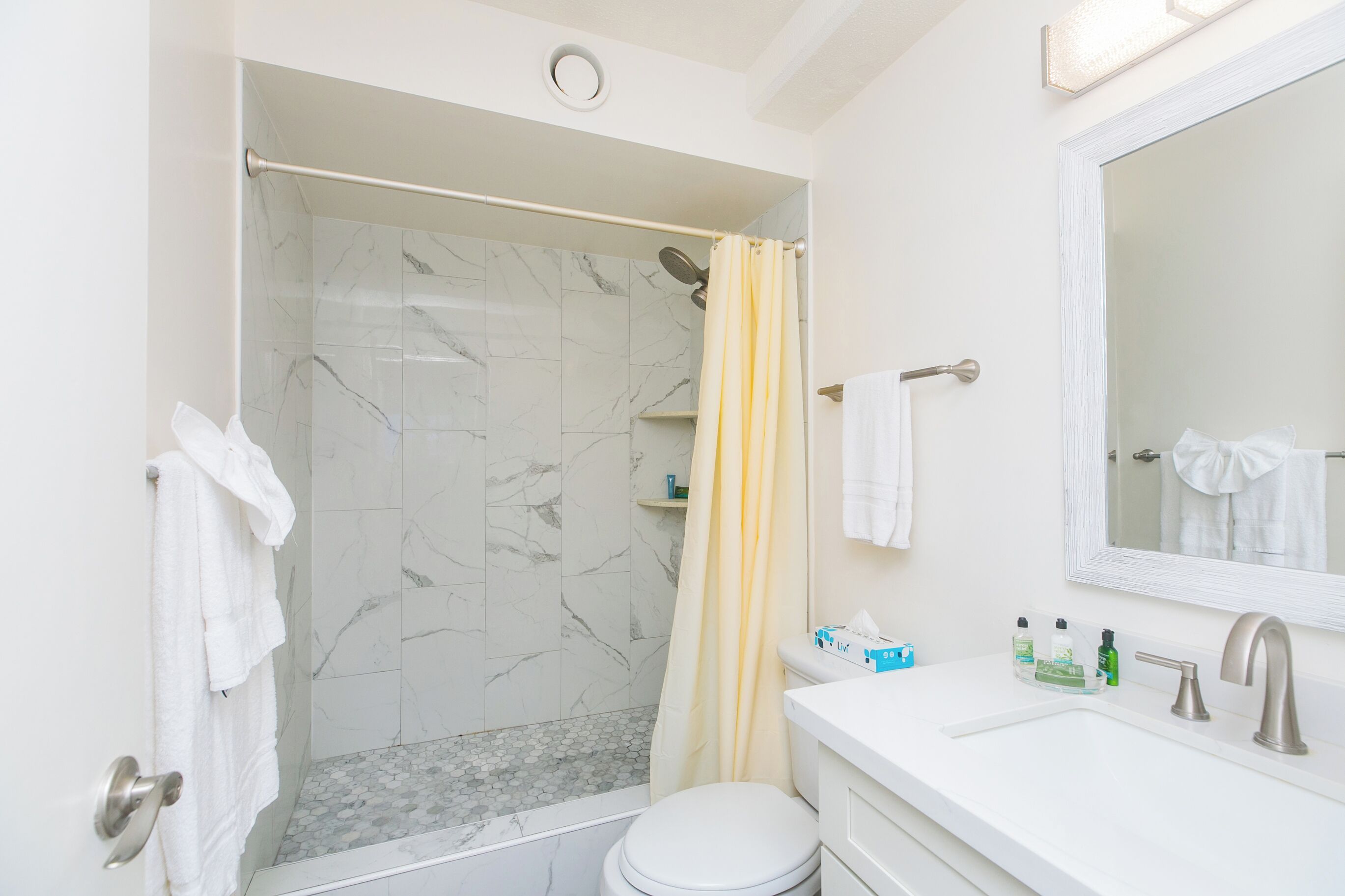 A bathroom with a shower, toilet, sink, and a mirror.