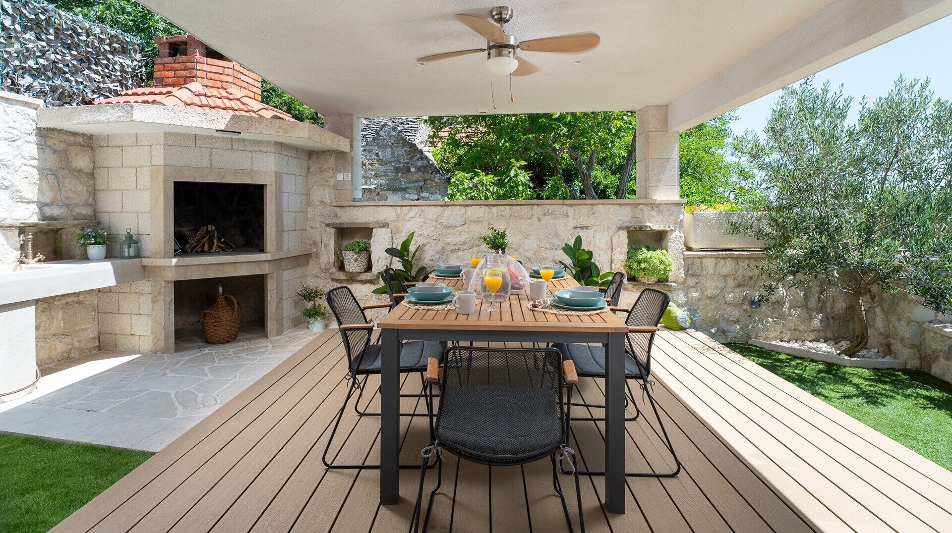 Eine Terrasse im Freien mit Kamin aus Stein, einem Tisch für vier Personen und einem Deckenventilator.