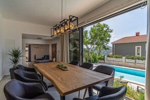 Ein moderner Essbereich mit einem Holztisch und schwarzen Stühlen, mit Blick auf einen Swimmingpool und eine schöne Aussicht auf ein Haus und Bäume.