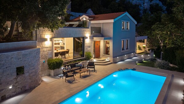 Ein modernes Haus mit Swimmingpool, Sitzgelegenheiten im Freien und einer gut beleuchteten Eingangsparte.