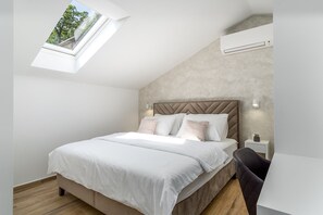 Ein modernes Schlafzimmer mit Dachfenster, einem Bett mit weißer Bettwäsche, einem Kopfteil, Nachttischlampen und einem kleinen Nachttisch mit Pflanze.