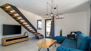 Un soggiorno moderno con una scala, un'ampia televisione, un divano blu e un tavolino in legno.
