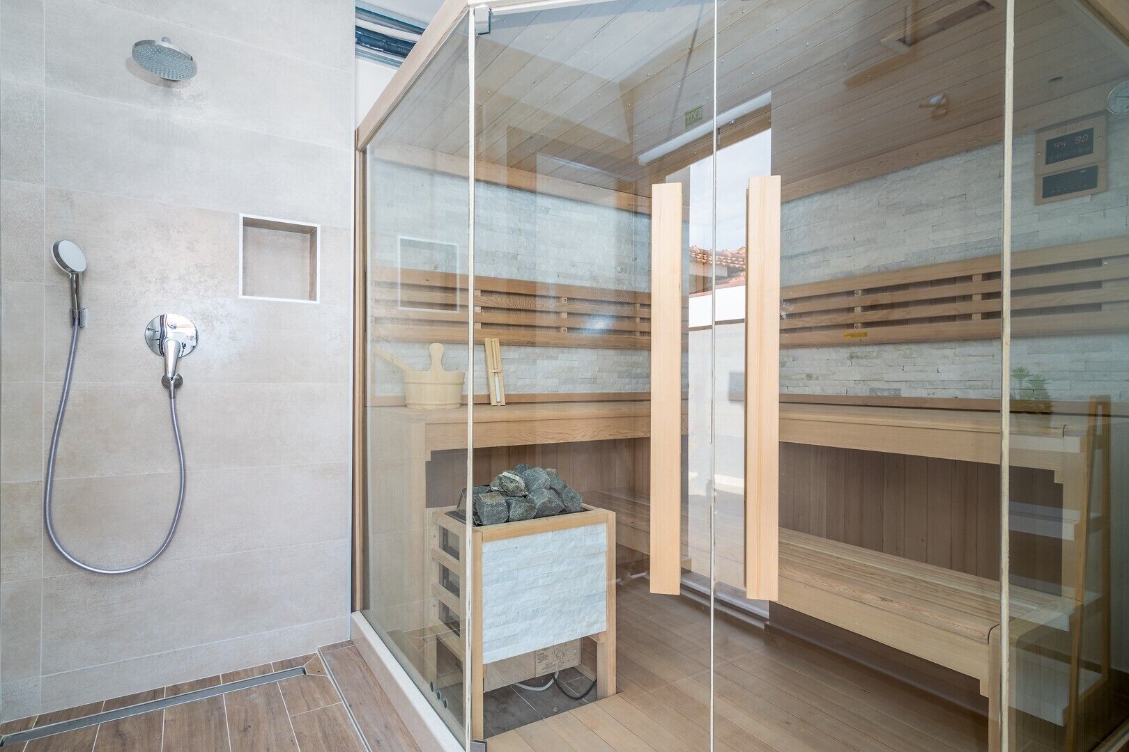 Een sauna met een glazen wand, houten banken en een doucheruimte.