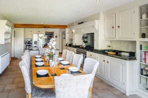 Une cuisine spacieuse avec des meubles blancs, une table à manger en bois pour six personnes et un îlot central doté d’un évier.