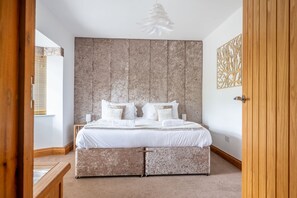 A bedroom with a large bed, a wooden headboard, a wall art piece, and a wooden door. - Grace Cottage, Heacham, Norfolk (Heacham)