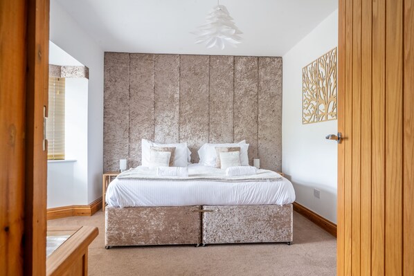A bedroom with a large bed, a wooden headboard, a wall art piece, and a wooden door. - Grace Cottage, Heacham, Norfolk (Heacham)
