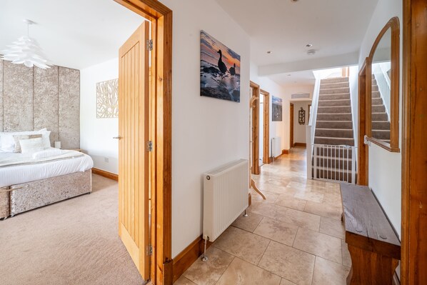 A bedroom with a bed, a wooden door, a radiator, and a hallway leading to a staircase. - Grace Cottage, Heacham, Norfolk (Heacham)