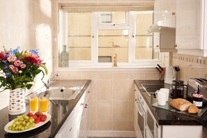 A kitchen with a window, a sink, a stove, and a countertop with a loaf of bread and a jar of jam.