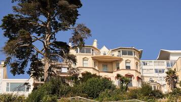 A multi-story building with a prominent tree in the foreground, balconies, and a clear sky.