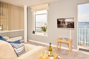 A living room with a view of the sea, a sofa, a small table with snacks and wine, and a framed photograph on the wall. - Bayfort Sea Studio (Torquay)