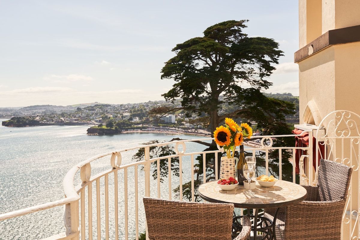 A balcony with a table, chairs, and a vase of sunflowers.