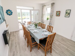 Un coin repas avec une table dressée pour six personnes, des chaises en bois et une vue sur un espace extérieur, accessible par une porte vitrée.