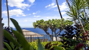 Vista de una zona costera con cielo despejado, palmeras y un edificio con techo que da al mar.