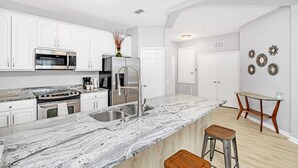 A modern kitchen with white cabinetry, stainless steel appliances, and a marble countertop. - Luxurious 3BD Home Close to Convention Center and Themed Parks! #3vc209 (Orlando)