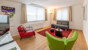 Un salon moderne avec un canapé rouge, un canapé gris, un fauteuil vert, un tapis rouge et un lampadaire.