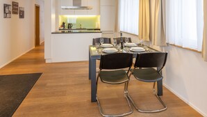 Un espace repas moderne avec une table en verre, des chaises noires et une cuisine en arrière-plan.