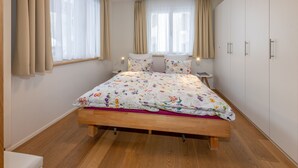 Une chambre à coucher avec un lit en bois, une literie à motifs floraux, deux tables de chevet avec des lampes et une armoire.