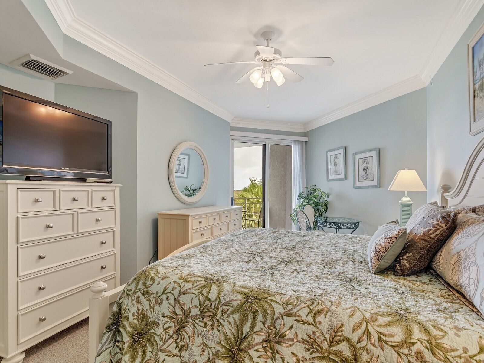 Une chambre avec un lit, une commode, une télévision, un ventilateur de plafond et un balcon avec vue.