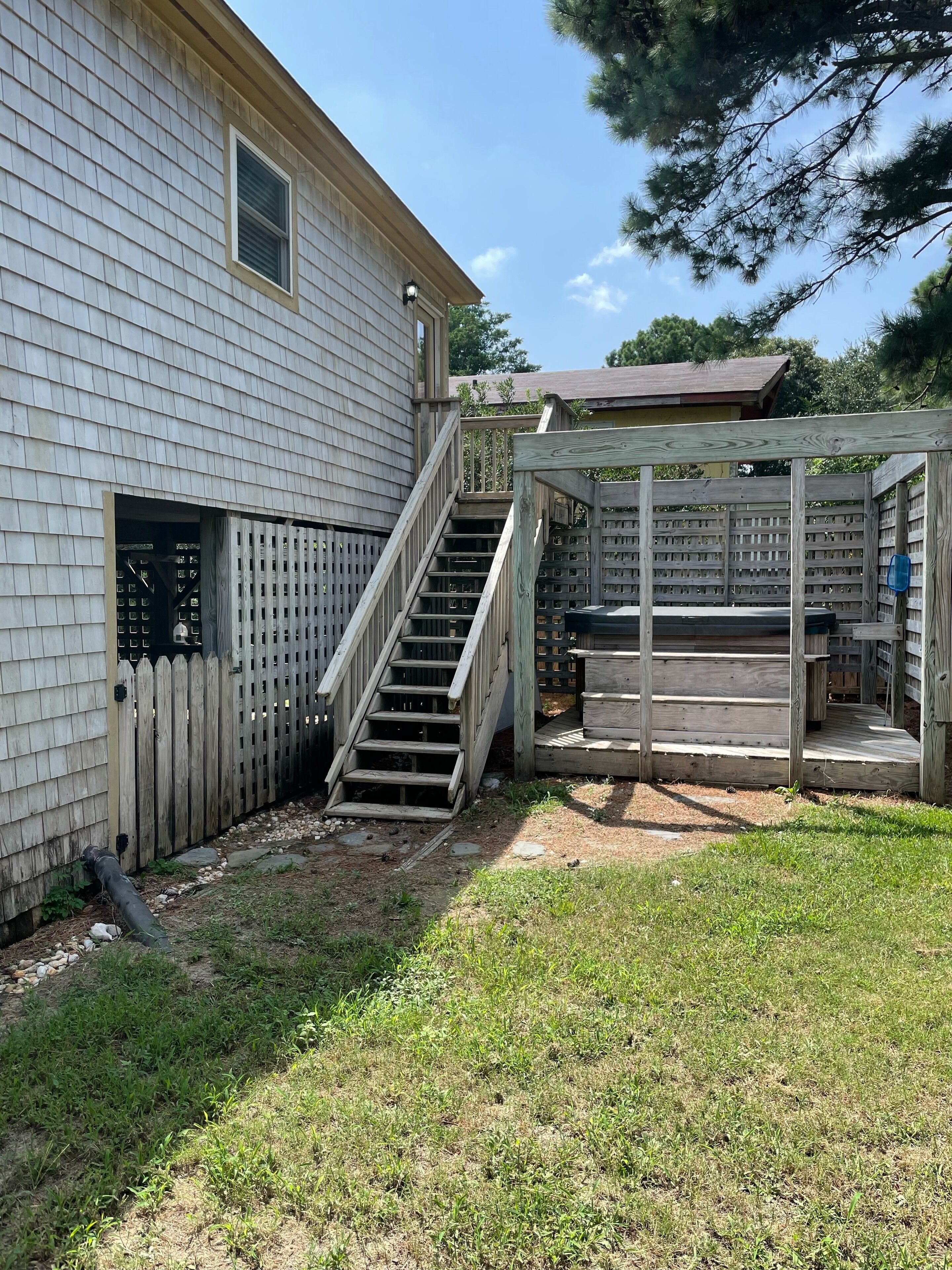 A wooden deck with a staircase leading to a covered area, surrounded by a wooden fence and a house with a window and a door.