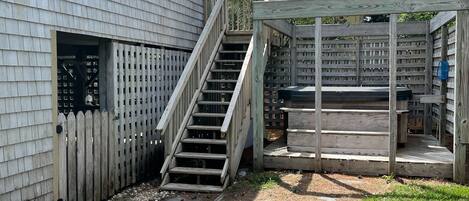 A wooden deck with a staircase leading to a covered area, surrounded by a wooden fence and a house with a window and a door.