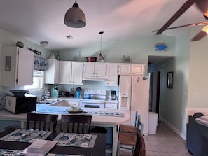 A kitchen with white cabinets, a stove, a refrigerator, and a dining area with a table and chairs. - Pet friendly 3 Bed/ 2 Bath Soundside retreat in OBX with Hot Tub & Enclosed yard (Kill Devil Hills)