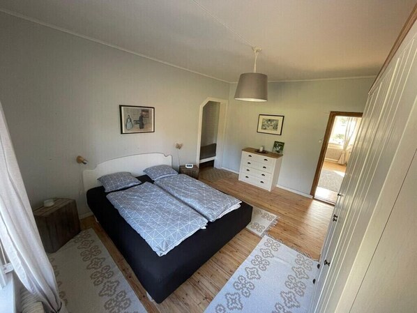 A bedroom with a double bed, bedside tables, a dresser, and a hanging lamp.