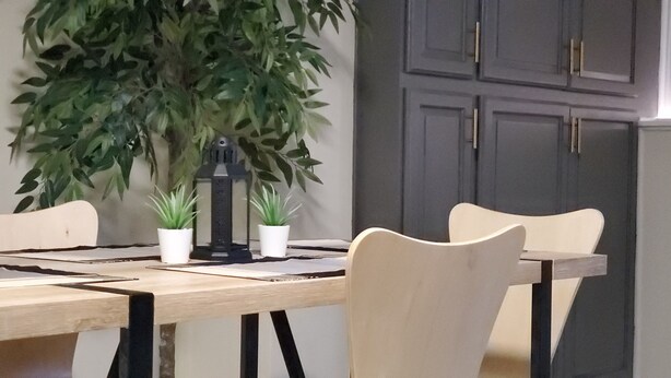 A dining area with a wooden table, four chairs, and two potted plants.