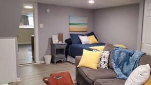 A bedroom with a bed, bedside table, and a nightstand. There is a door to another room and a hallway leading to a bathroom.