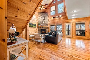 Un intérieur spacieux de chalet en bois, avec une cheminée en pierre, des planchers en bois et de grandes fenêtres.