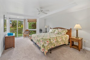 A bedroom with a bed, a nightstand, a chair, a fan, and a view of the outdoors.