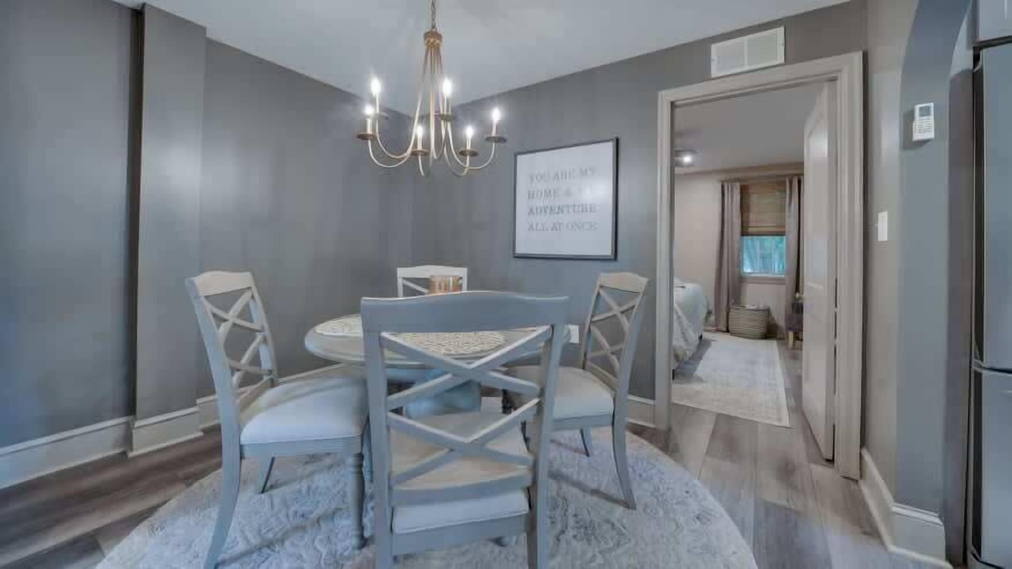 A dining area with a chandelier, a framed inspirational quote, and a view into the adjacent room.
