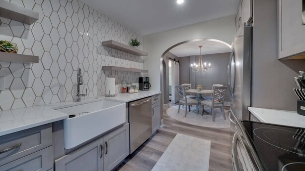 Een moderne keuken met witte kasten, een inbouwoven en een eethoek met een ronde tafel en stoelen.