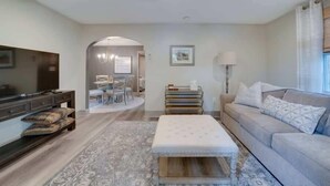 Een moderne woonkamer met een flatscreen-televisie, een bank, een salontafel en een eethoek met stoelen en een tafel.