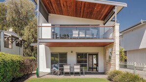 Une maison moderne à deux étages, dotée d’un balcon, de grandes fenêtres et d’un jardin bien entretenu.
