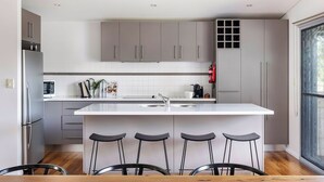 Une cuisine moderne avec des meubles gris, un îlot central blanc doté de tabourets, un réfrigérateur en acier inoxydable et une fenêtre laissant entrer la lumière naturelle.