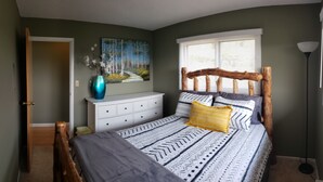 Ein Schlafzimmer mit einem Bett, einer Kommode, einem Gemälde und einem Fenster mit Jalousien.